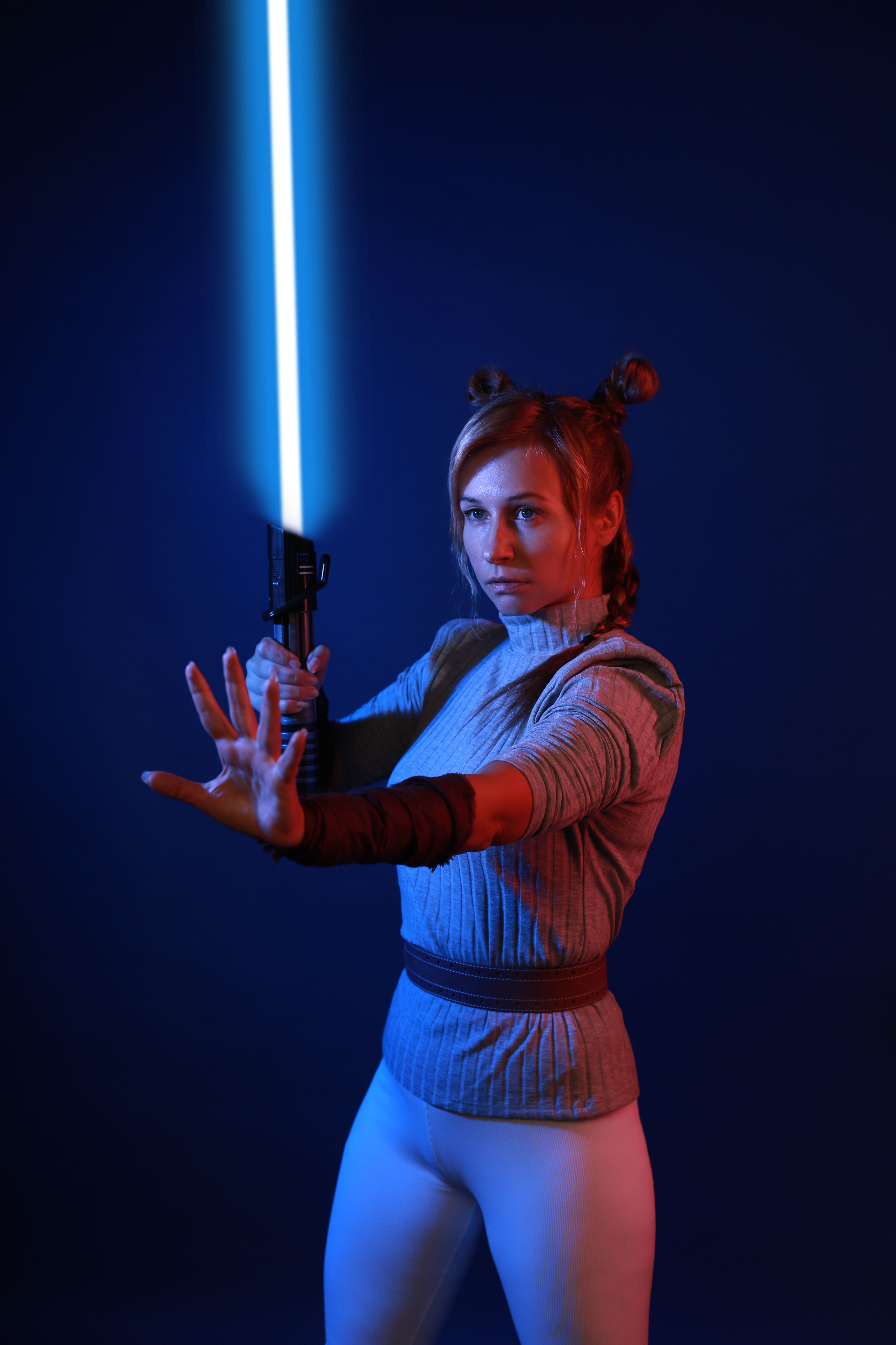 A woman dressed as a warrior holding a blue light sword against a blue background.