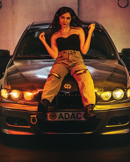 Young Woman in Headphones Sitting on the Hood of a BMW