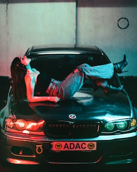 Stylish woman in boots lounging on a BMW under urban lights.