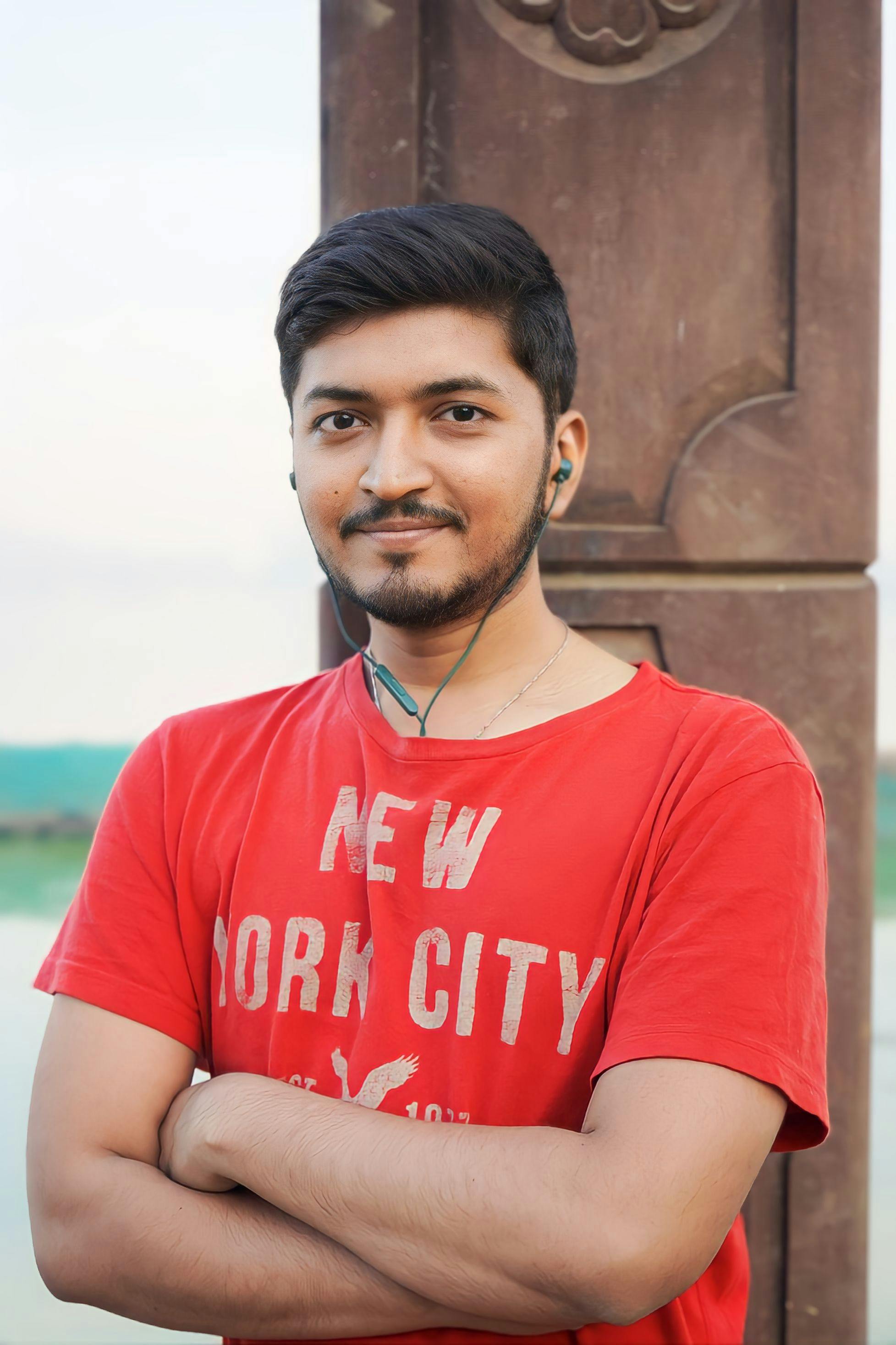 Portrait of a man in a red t-shirt with earphones, smiling and standing outdoors.