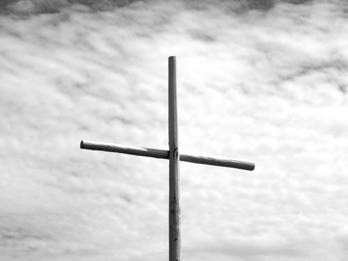 Free Monochrome image of a wooden cross silhouetted against a cloudy sky symbolizing spirituality and faith. Stock Photo