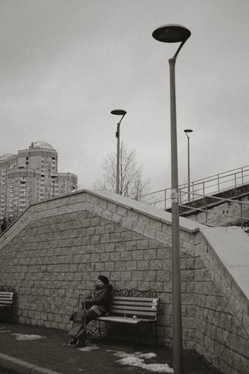 Free Elderly woman sits on a bench in winter urban setting, captured in black and white. Stock Photo