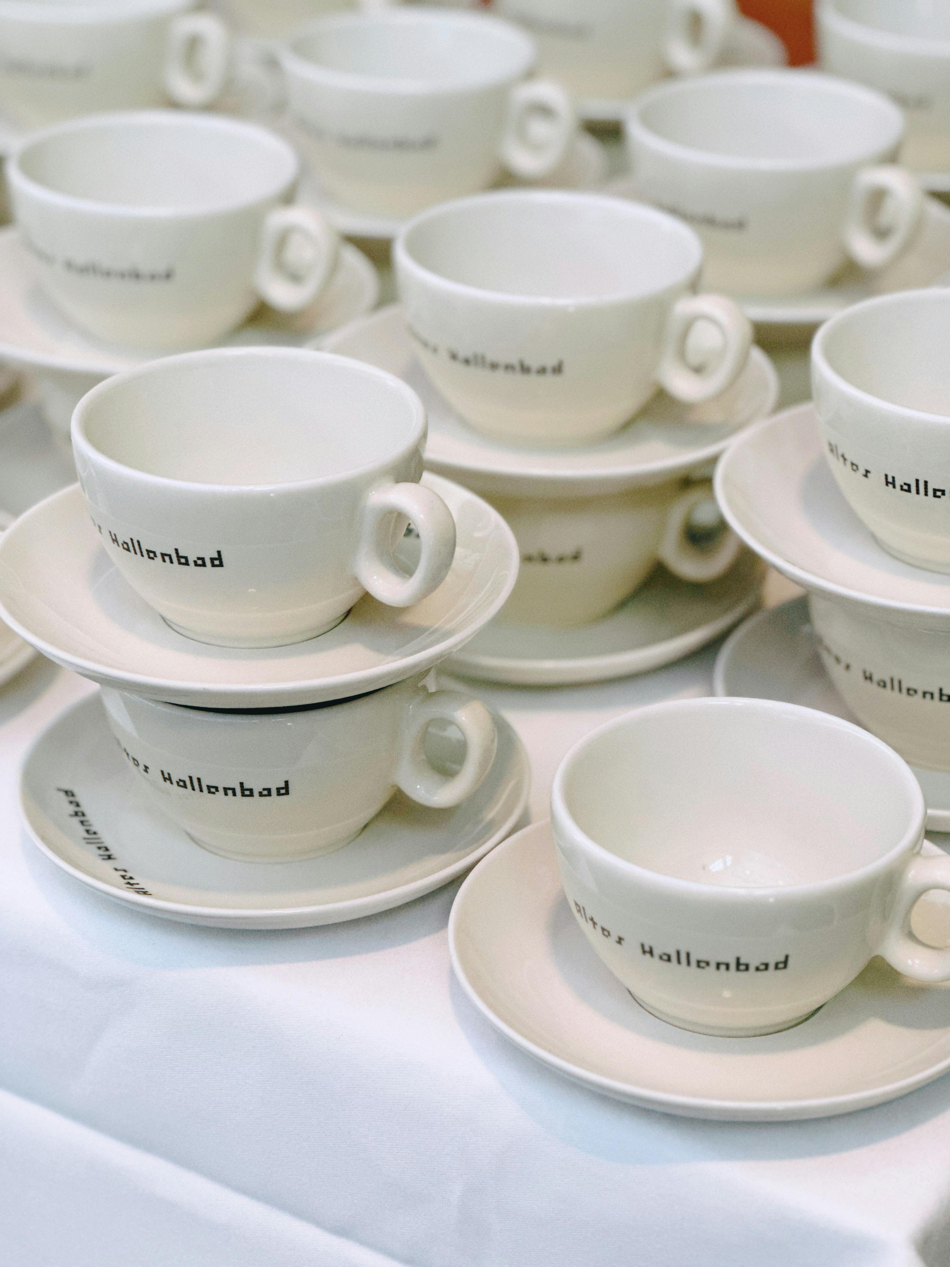 Multiple white cups and saucers neatly stacked on a table, perfect for event preparation.