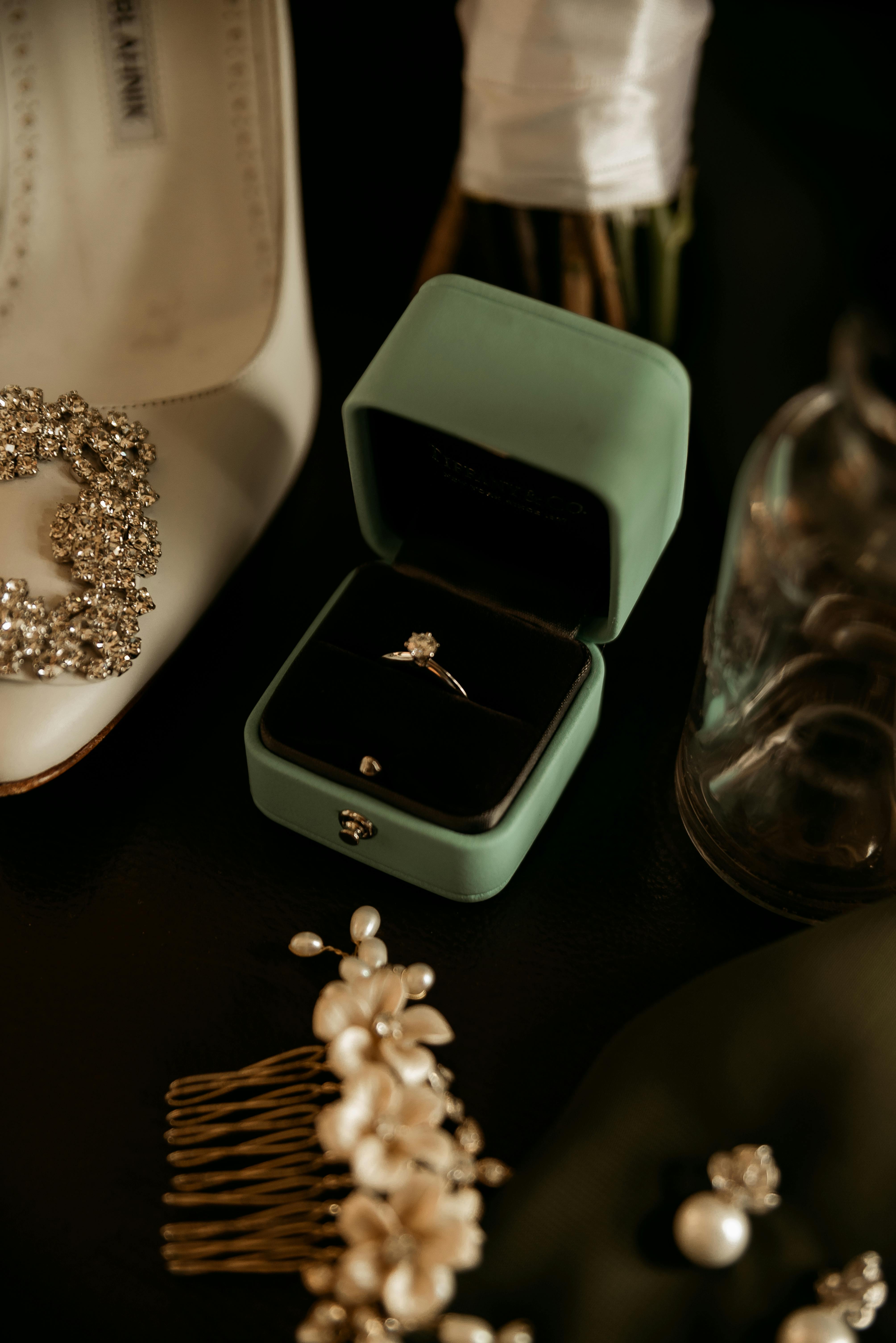 Luxurious diamond engagement ring in an elegant green velvet box, surrounded by wedding accessories.