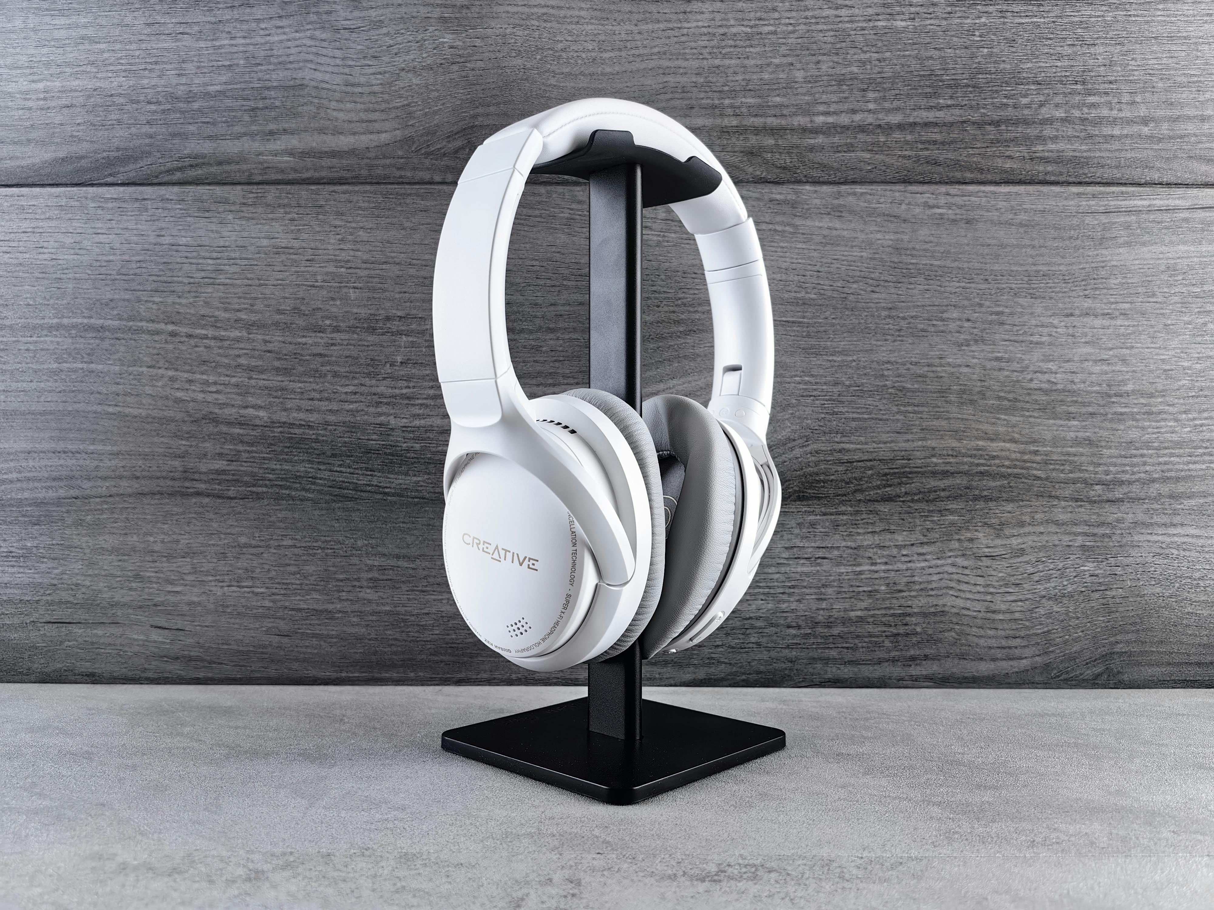 White headphones on a stand against a wooden background, showcasing modern audio equipment.