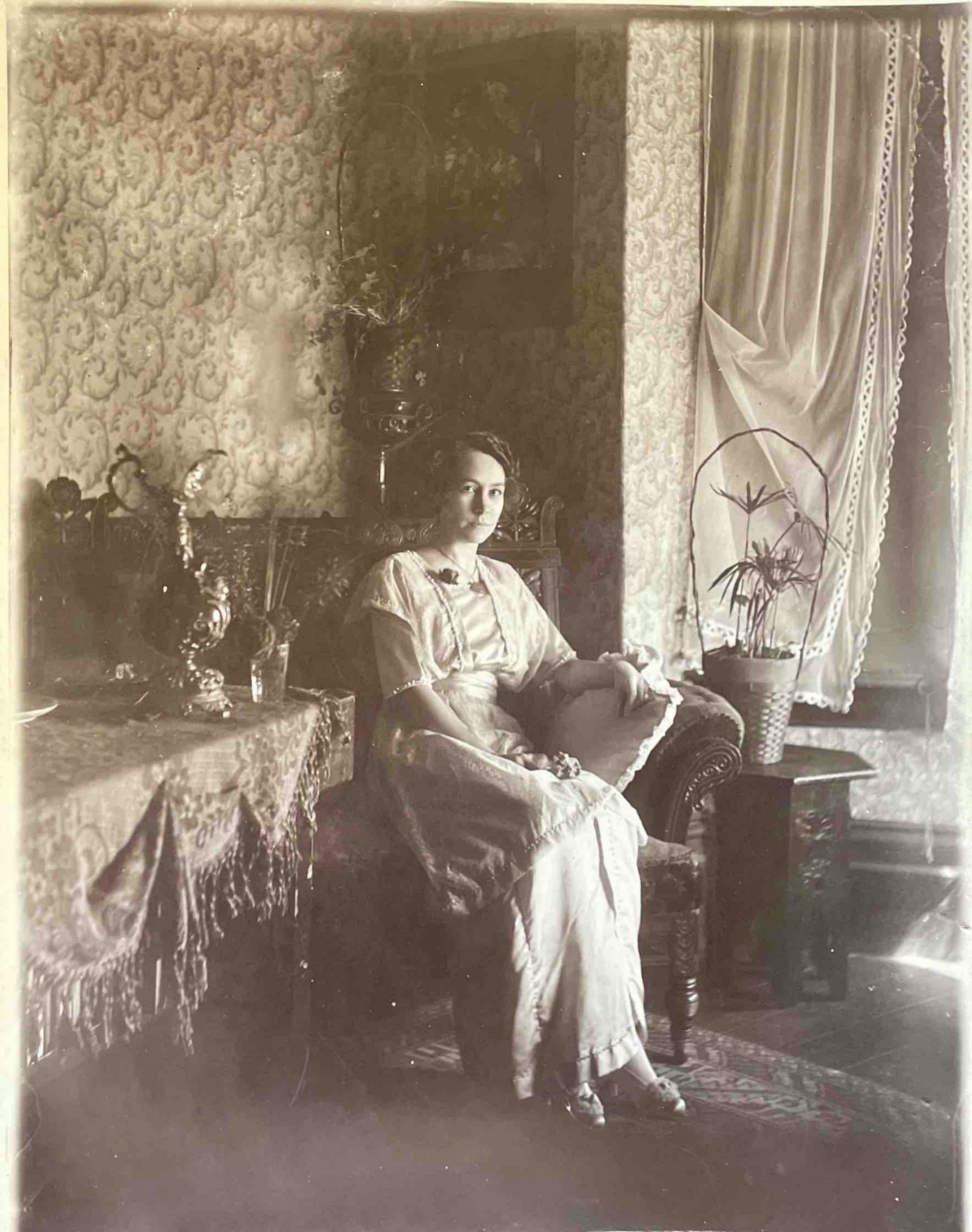 A sepia-toned vintage portrait of a woman sitting in an ornate interior setting.
