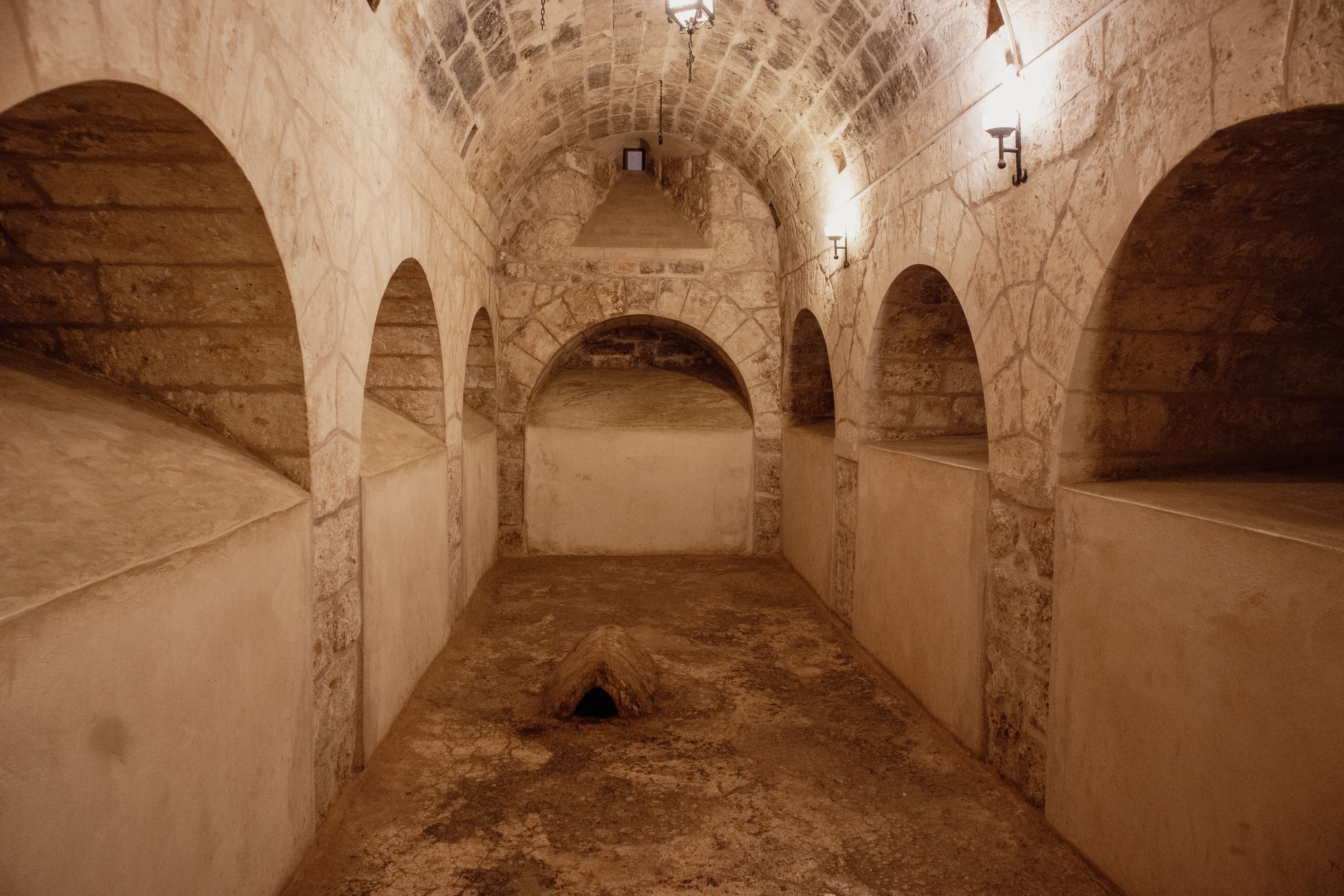 Sous-sol ancien à voûtes de pierre et arcades, vide et éclairé par une ouverture latérale.