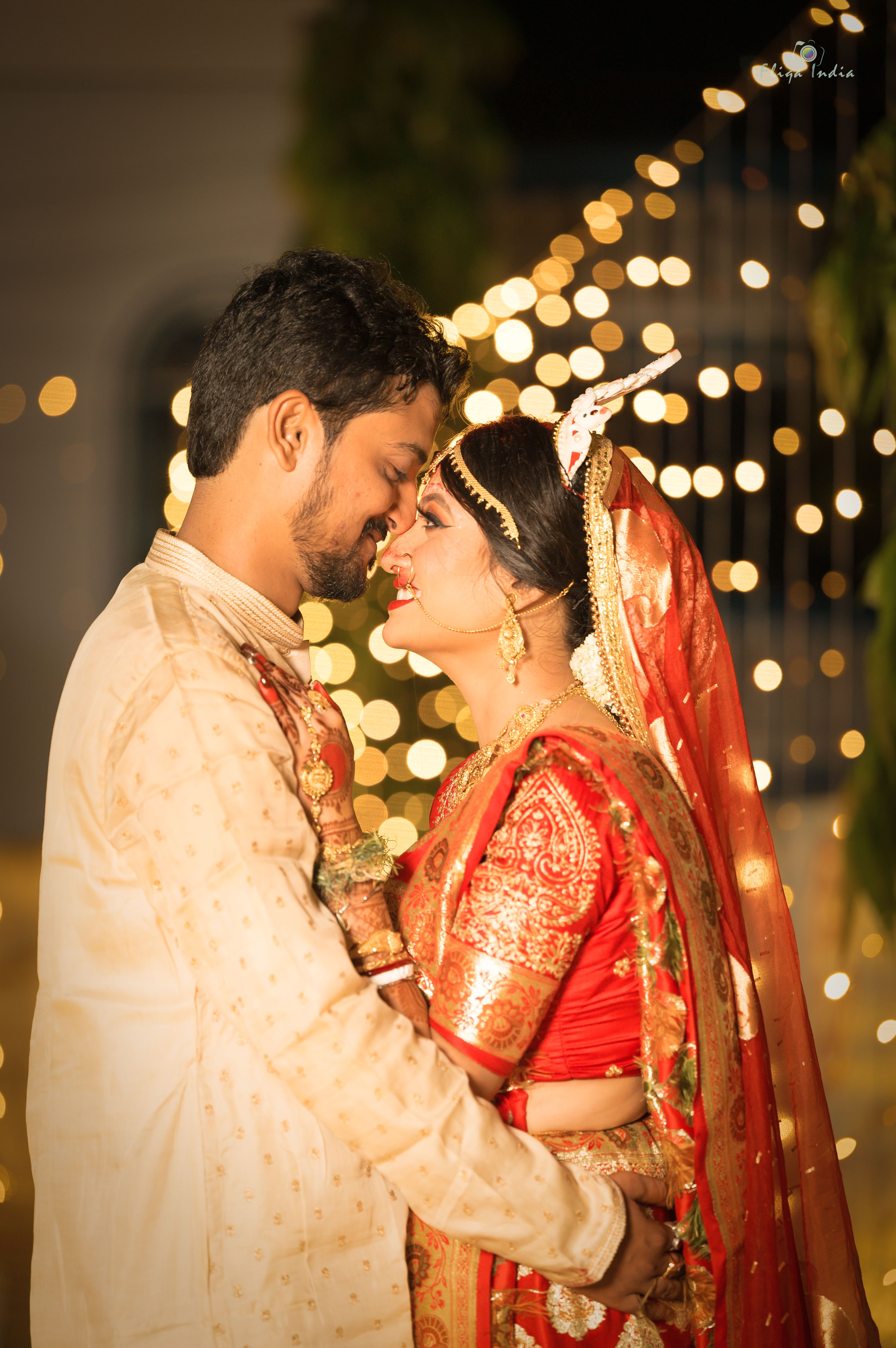 Bride and groom embracing during traditional Indian wedding ceremony under fairy lights.