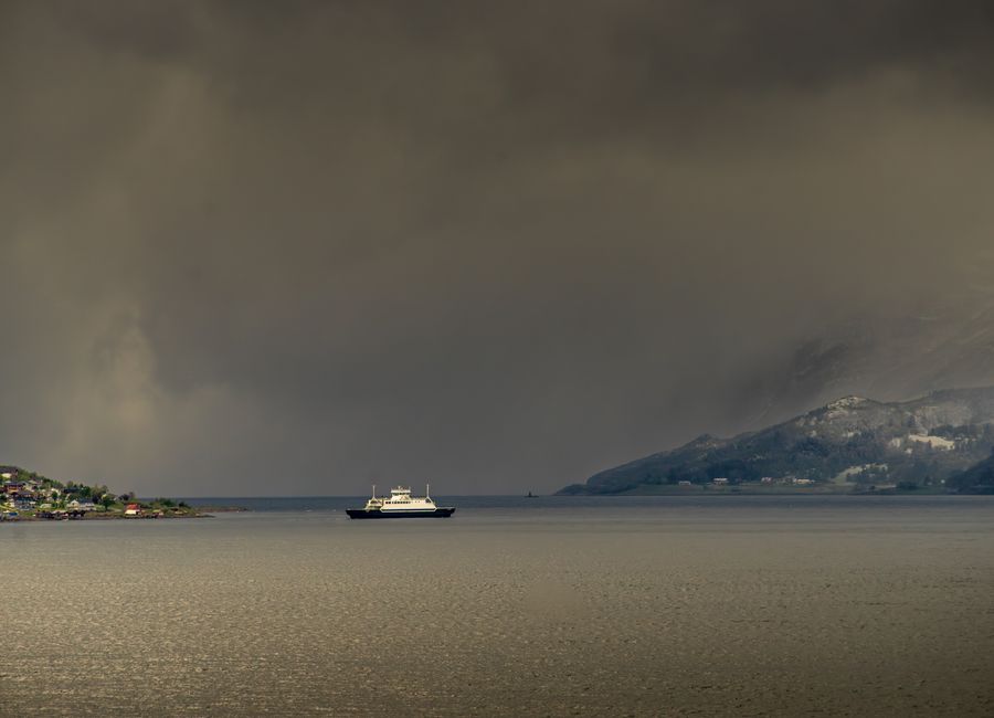 A ferry traversing the serene waters of Harstad, surrounded by dramatic skies and coastline in Norway.