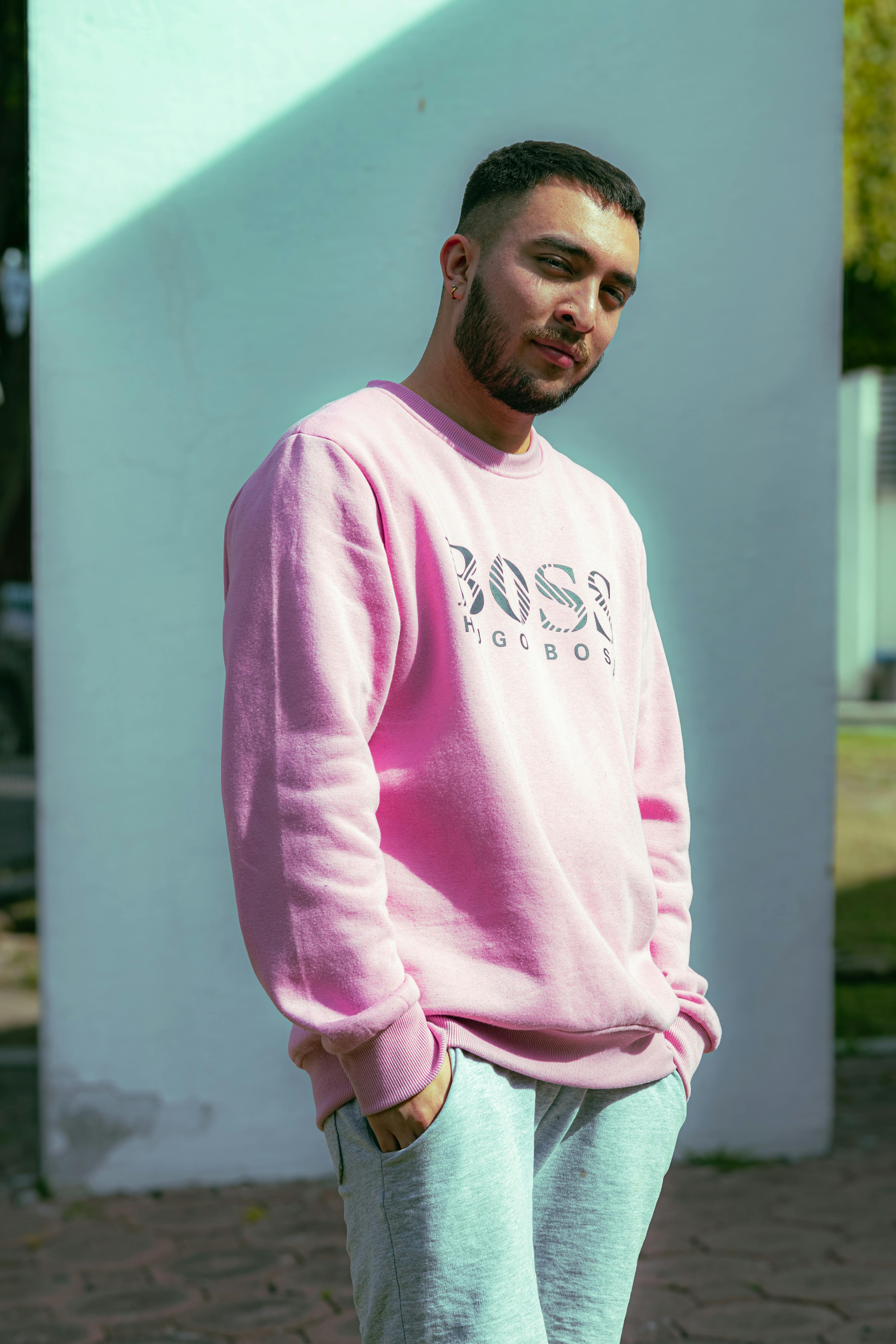 Portrait of a man in a pink sweatshirt posing outdoors, urban backdrop.