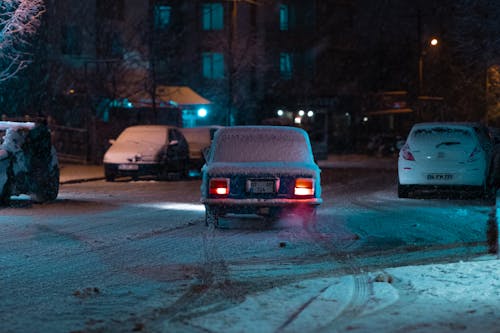 Snow-covered Car Driving on the Street at Night