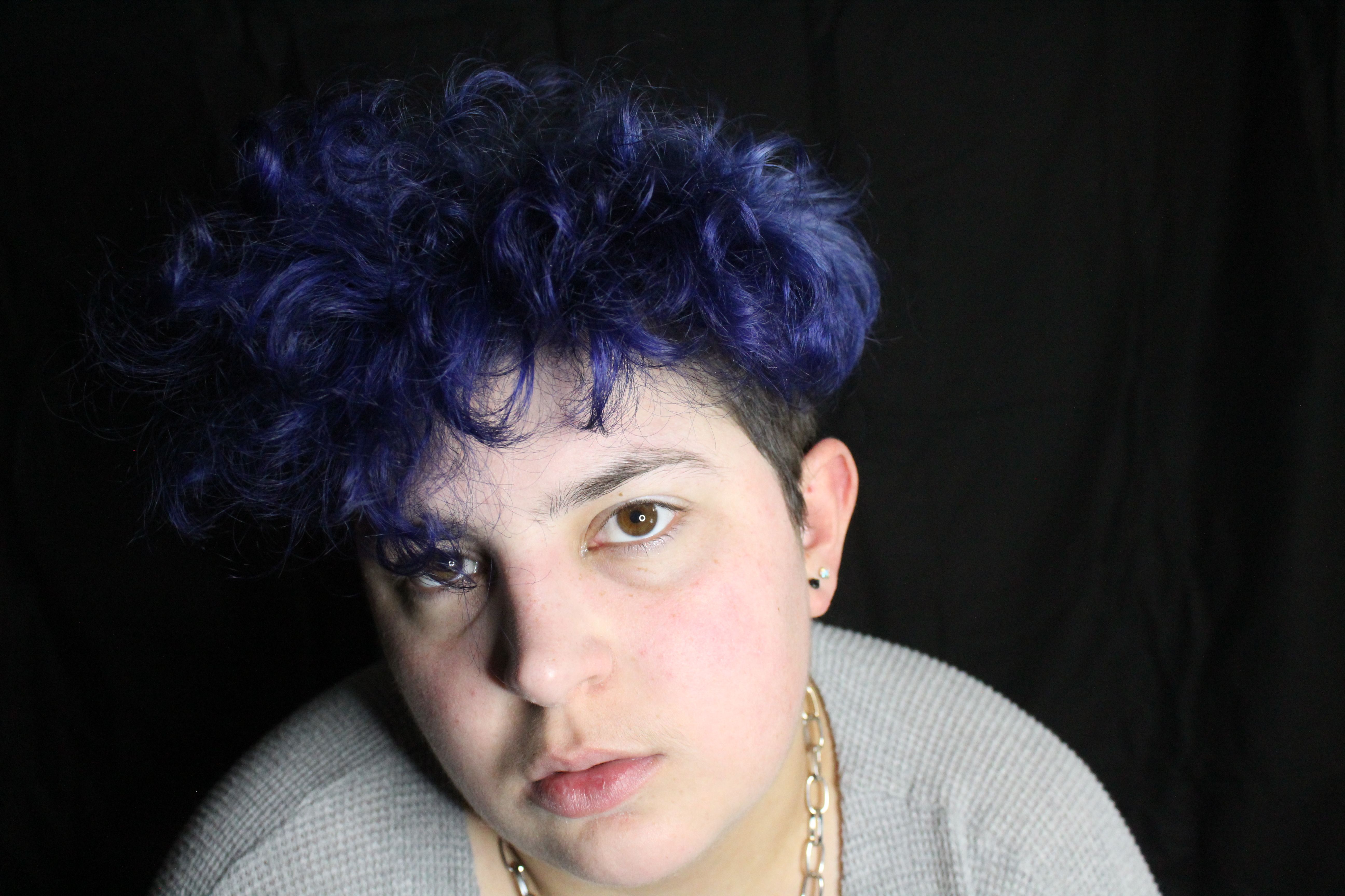 Close-up portrait featuring a person with striking blue curly hair and small earrings.