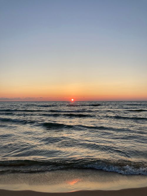 Free Peaceful ocean waves under a vibrant sunset sky creating a tranquil seascape. Stock Photo