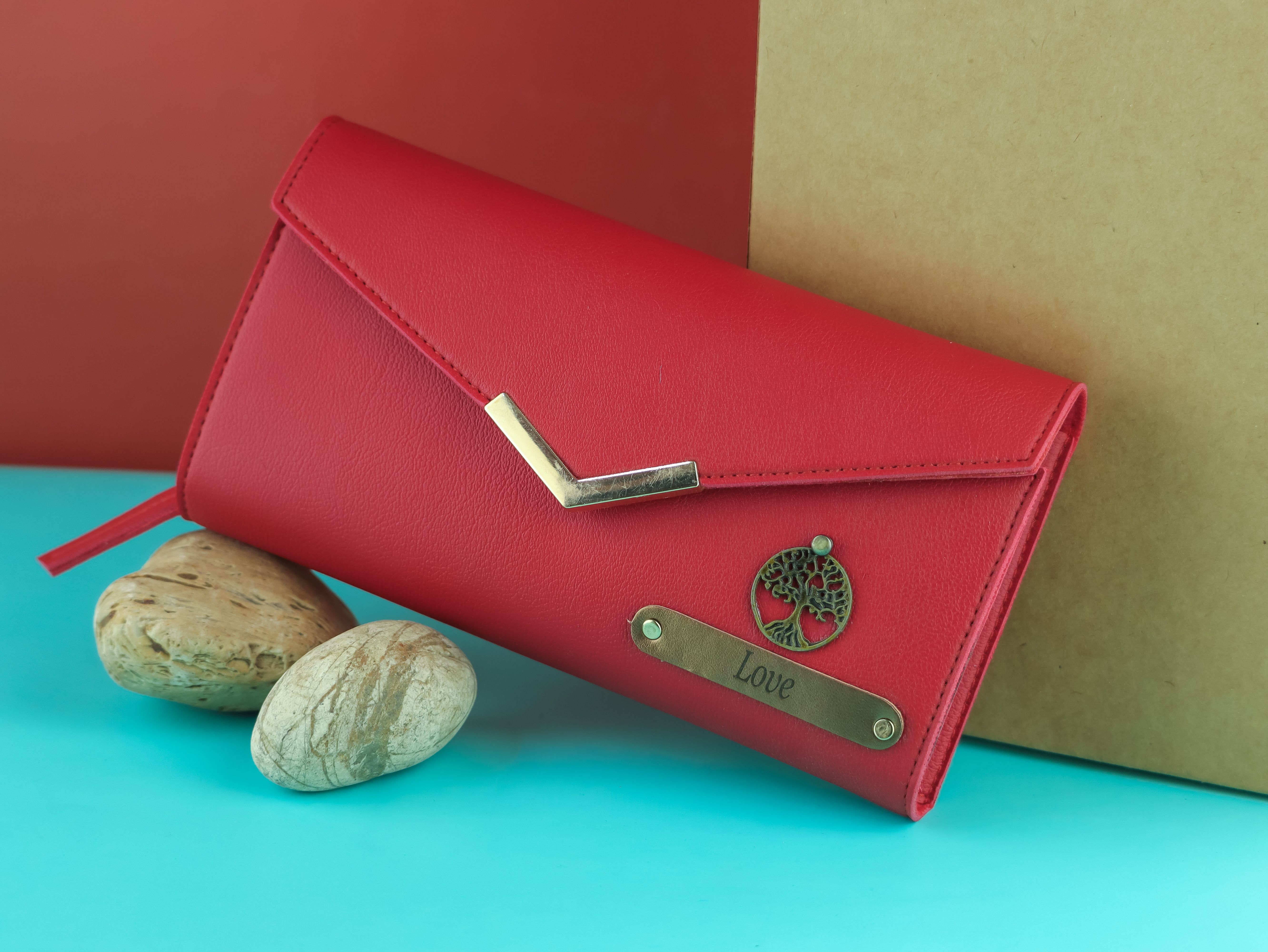 Elegant red wallet featuring a metal tree emblem and 'Love' inscription, posed on a turquoise and red background.