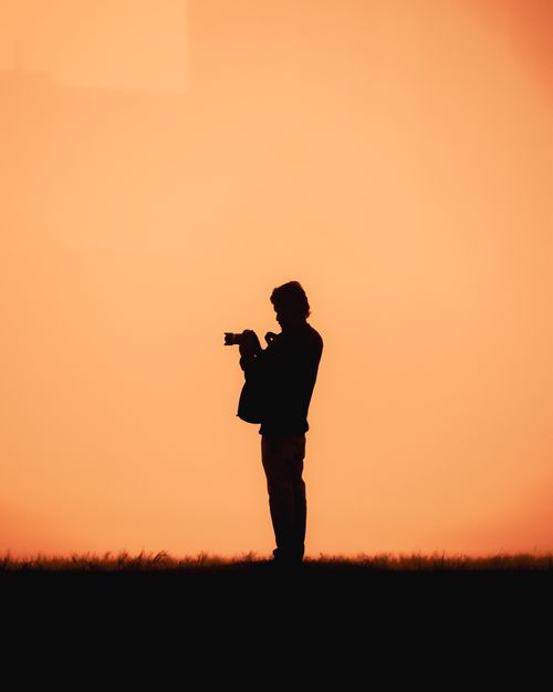 Free Silhouette of a photographer capturing the sunset in an open field, creating a dramatic and peaceful scene. Stock Photo