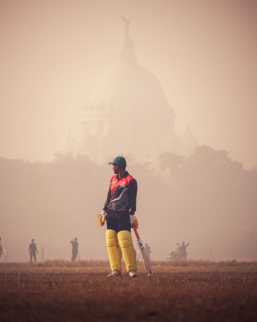 Cricket player standing on a misty field with a historic landmark visible in the background