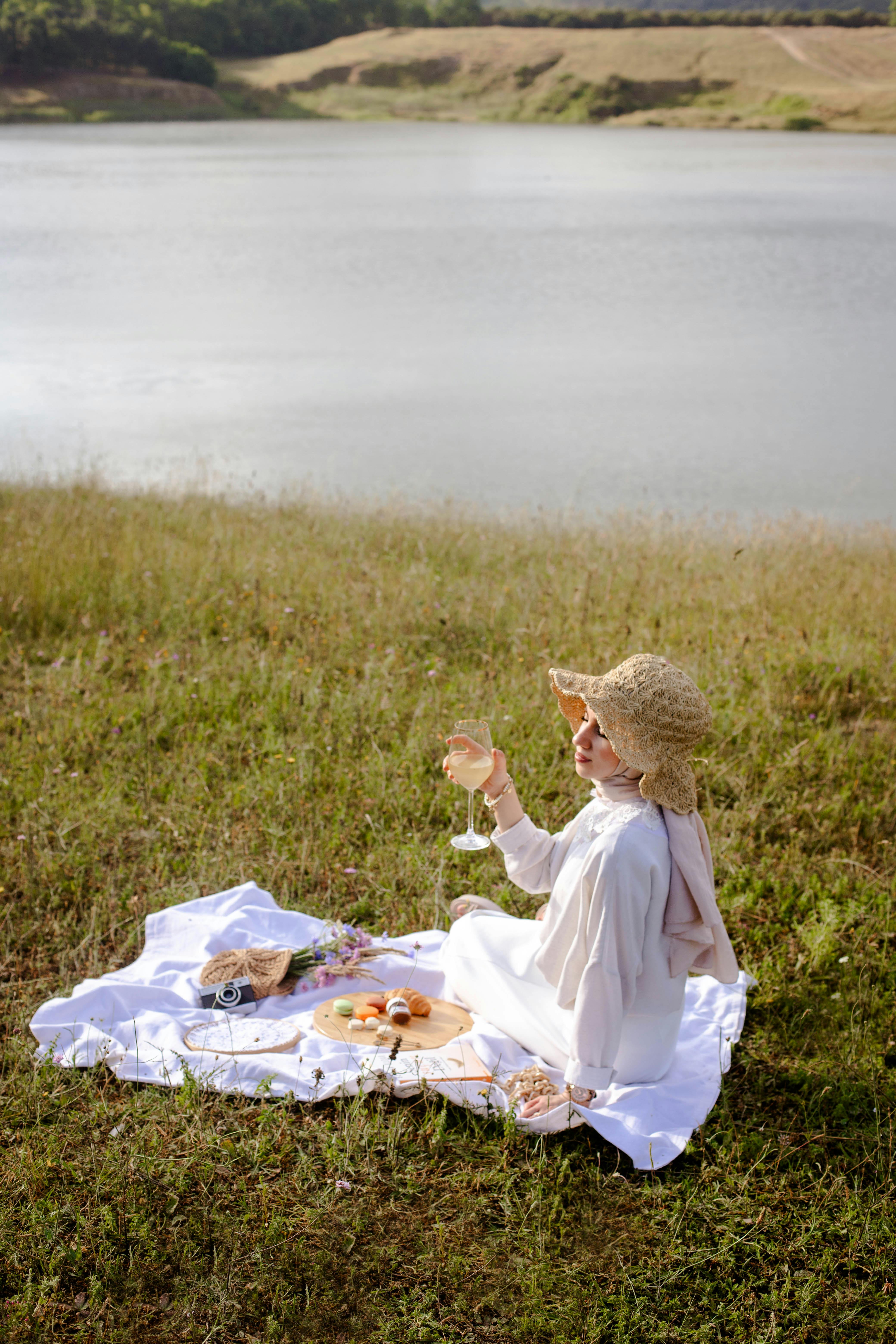 Woman enjoying a peaceful picnic with wine on a sunny summer day by the river.