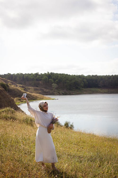 Woman in White Dress and Hijab Standing on Lakeshore