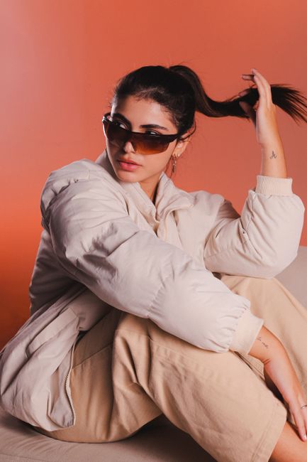 Stylish woman in sunglasses posing in a studio with a trendy outfit on an orange background.