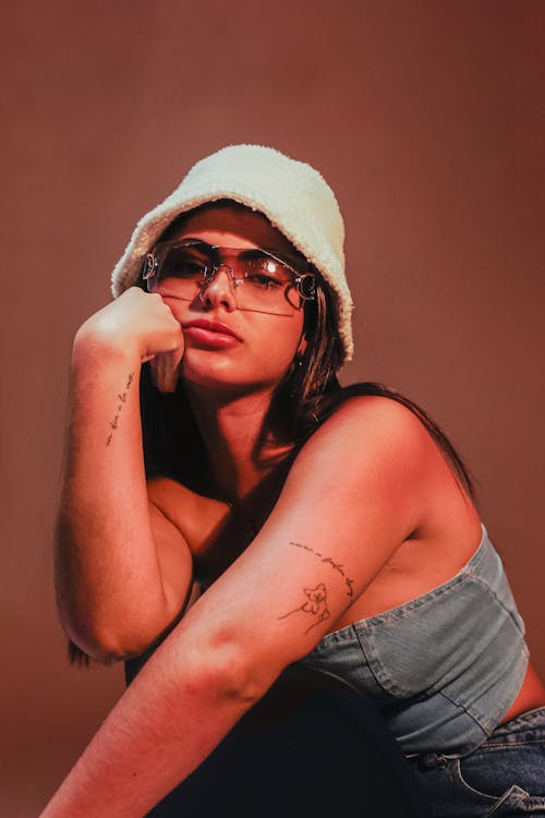 A woman in glasses and a hat sitting on a stool