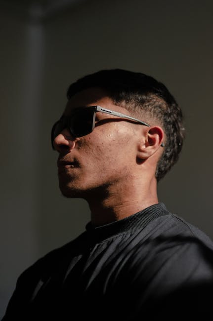 A stylish man wearing sunglasses in a dramatic side profile shot with shadows.