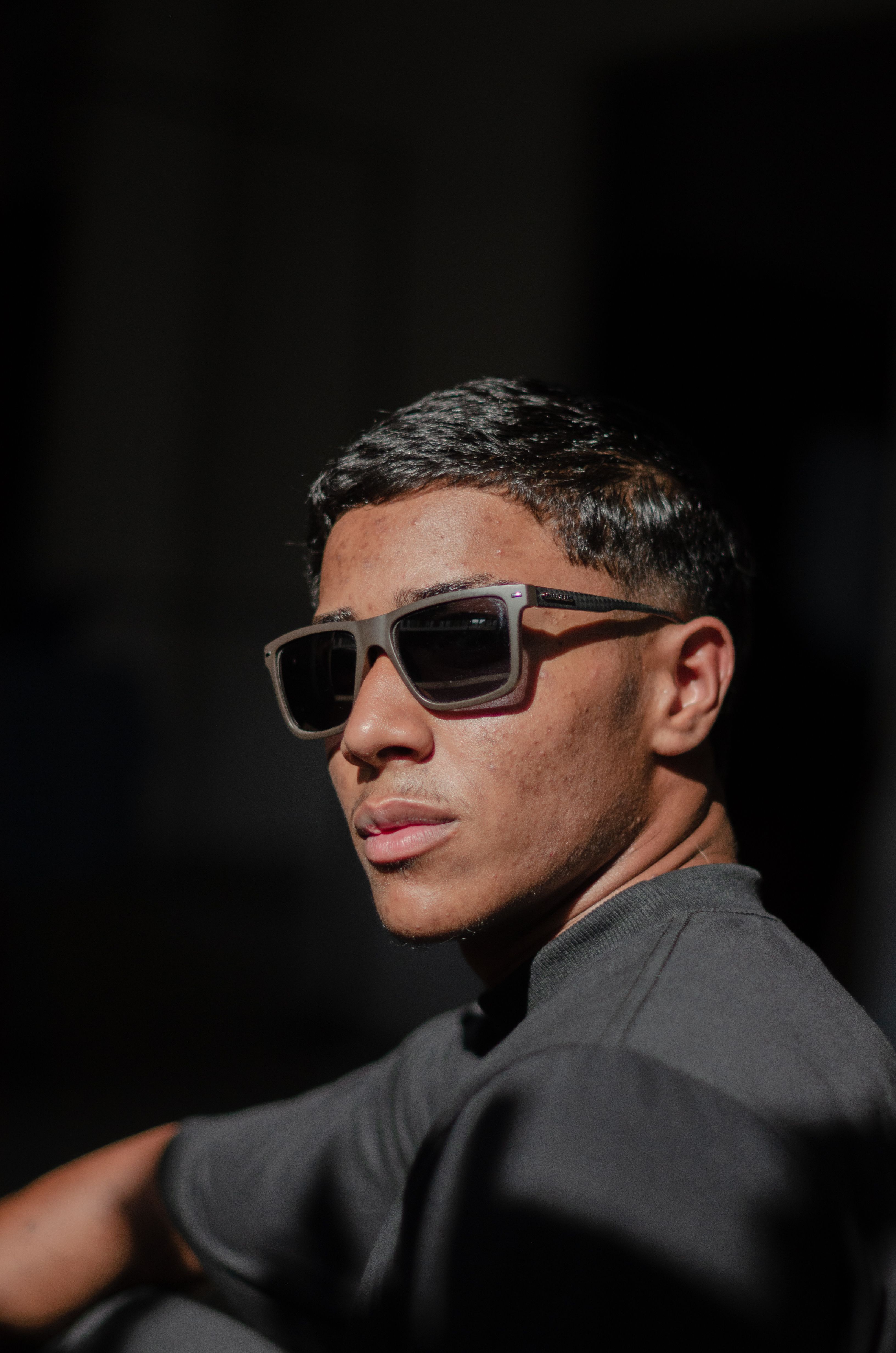 Portrait of a young man wearing sunglasses, enjoying sunlight in a stylish black t-shirt.