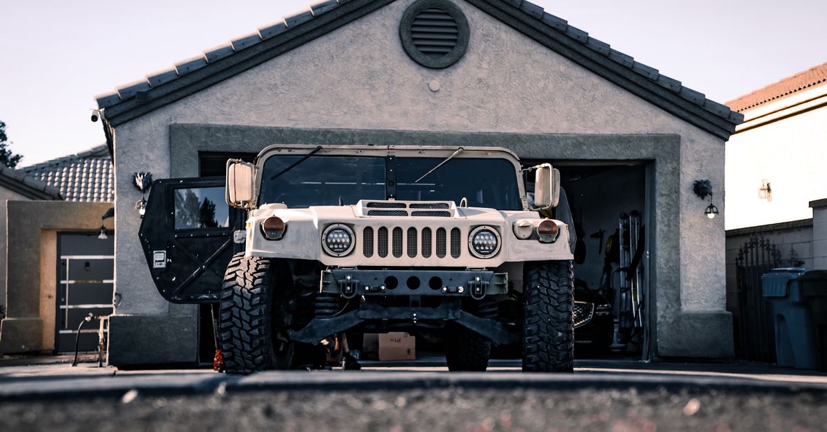 Heavy-duty military vehicle parked in a suburban garage driveway.