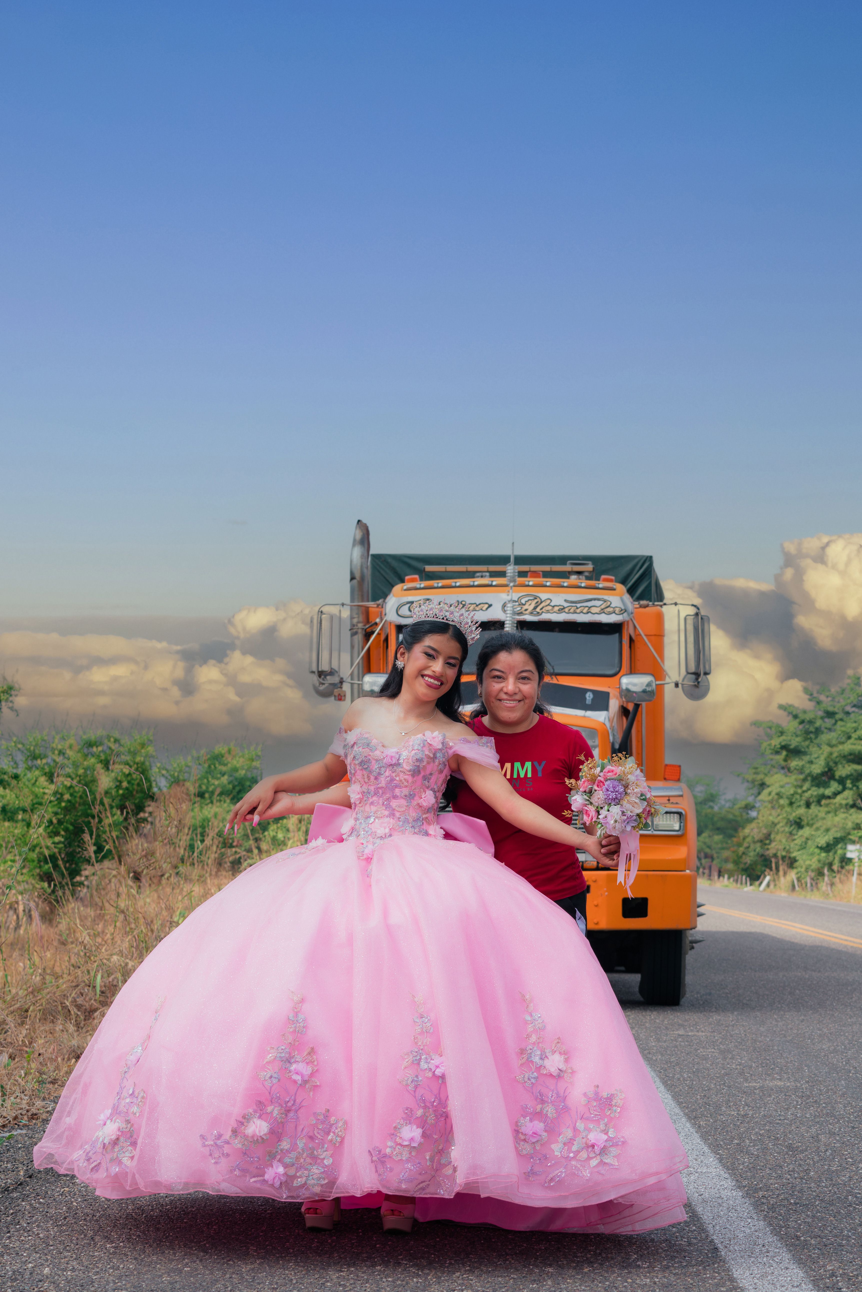 Joyful quinceañera posing with family by a vibrant truck, celebrating a special occasion outdoors.