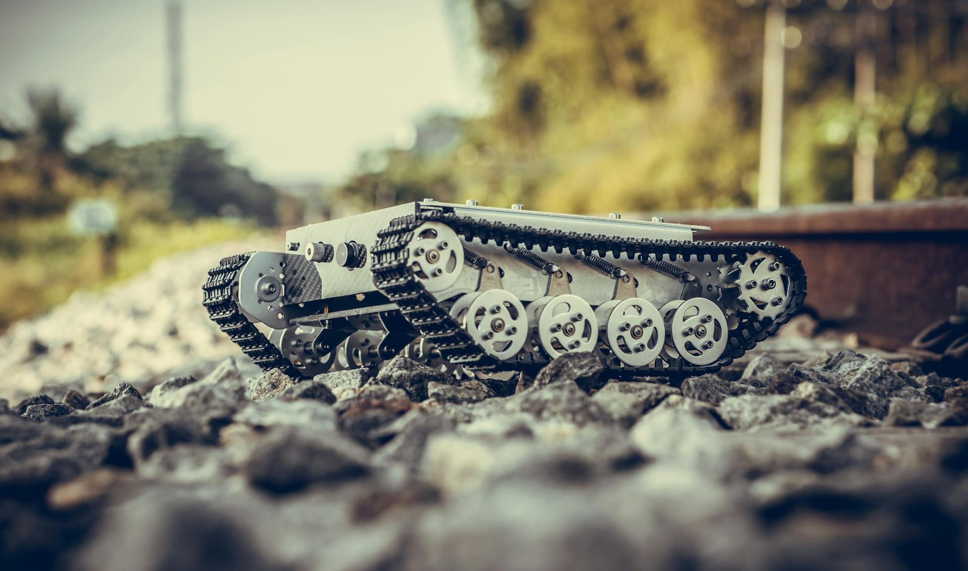 A miniature tank robot navigating through rocky terrain near railway tracks in Đà Nẵng, Vietnam.