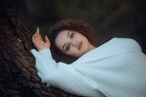 A woman in a white sweater leaning against a tree