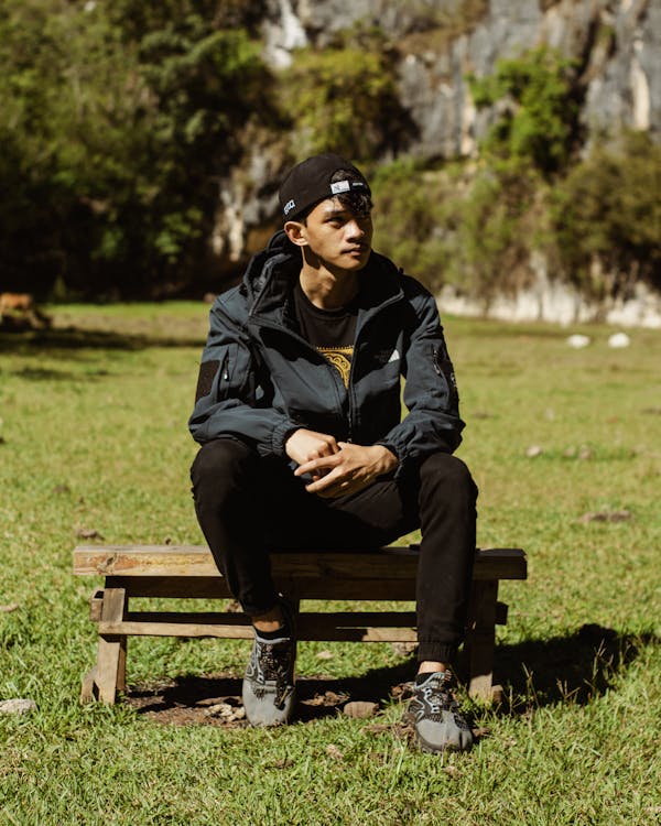 A Boy in a Jacket and Cap Sitting in a Park 