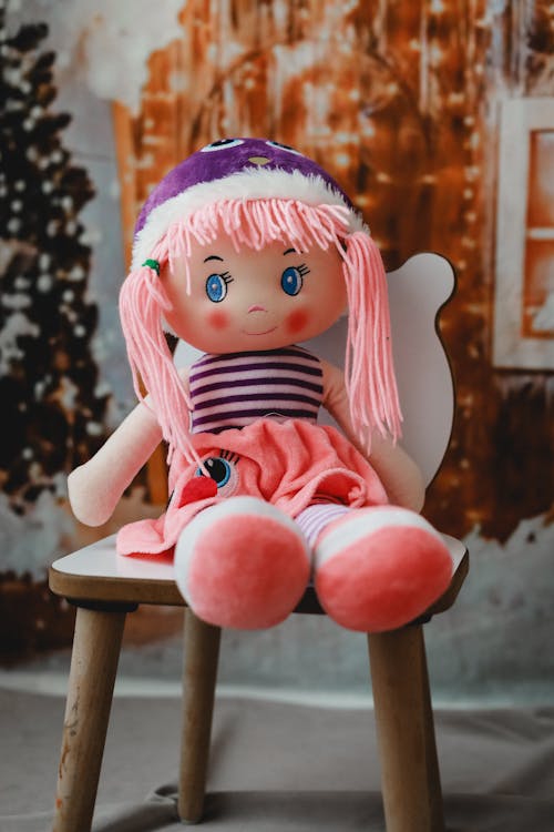 A Doll Sitting on a Small Chair on the Background of Christmas Decorations 