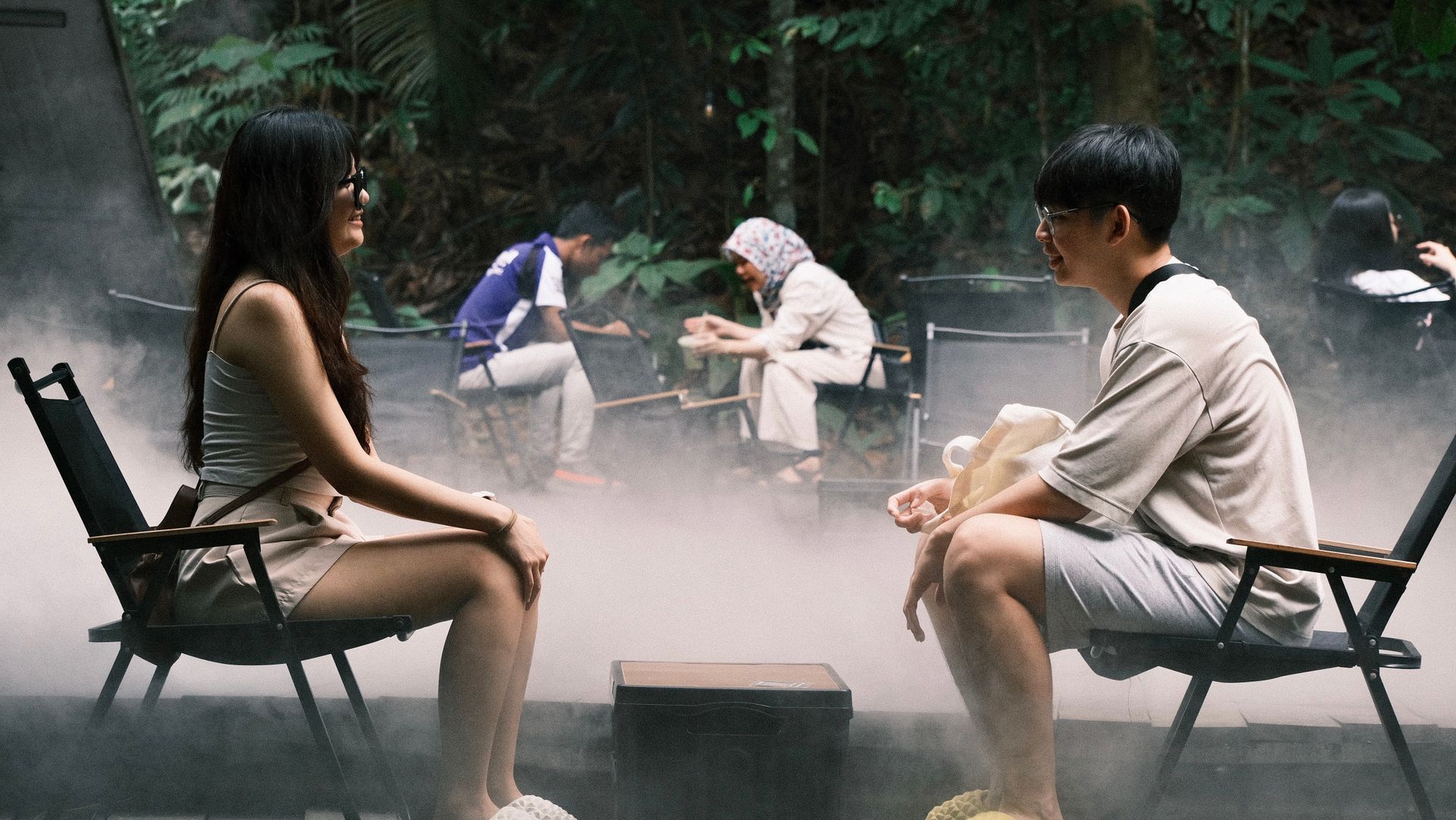 Two people enjoy a tranquil outdoor setting with mist and lush greenery.