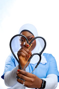 Female healthcare worker in hijab holding stethoscope in a heart shape on a white background.