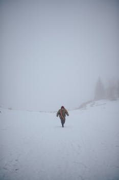 A person runs through a foggy, snow-covered landscape, dressed in warm winter clothing.