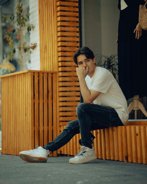 Free Stylishly dressed man in jeans and t-shirt sitting on a wooden structure outdoors. Stock Photo