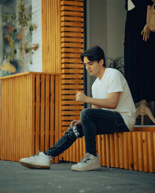 Free Man sitting outdoors with a camera in urban setting. Stock Photo