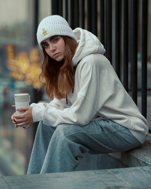 Woman in Hat and White Hoodie Sitting on Wall
