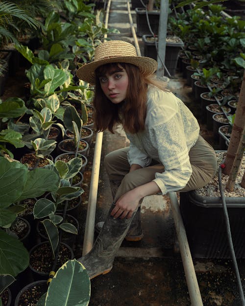 Gardener in White Shirt and Hat Sitting among Plants