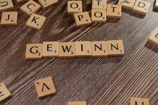Scrabble tiles spelling 'GEWINN' on a wooden surface, symbolizing victory.