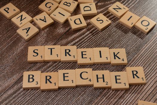 Wooden Scrabble tiles spelling 'Streik Brecher' on a wooden surface.