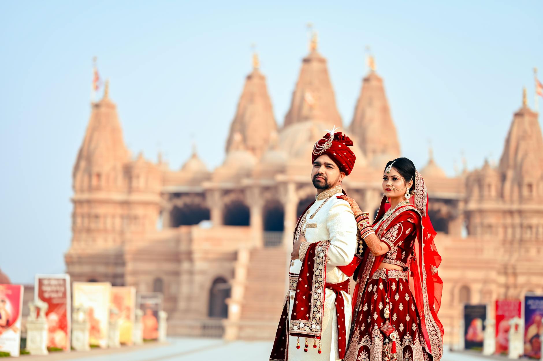 A couple in traditional Indian attire poses in front of a historic temple, showcasing cultural elegance.