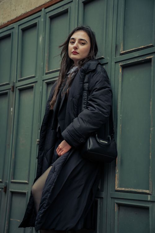 Free Portrait of a fashionable woman in a black jacket leaning against a vintage green wall. Stock Photo