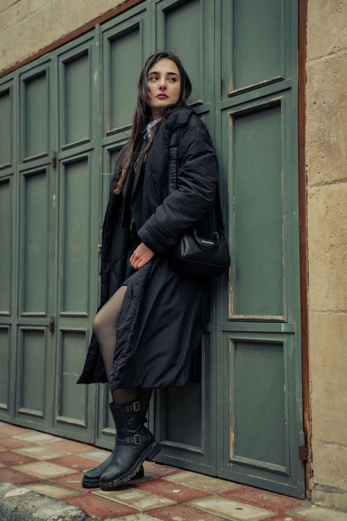 Free Elegant woman in a black coat poses against a green panel wall, showcasing fall fashion. Stock Photo