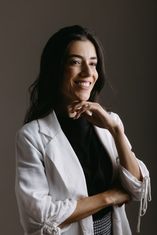 Free Portrait of a smiling businesswoman with a confident pose in a white blazer, indicating professionalism and style. Stock Photo