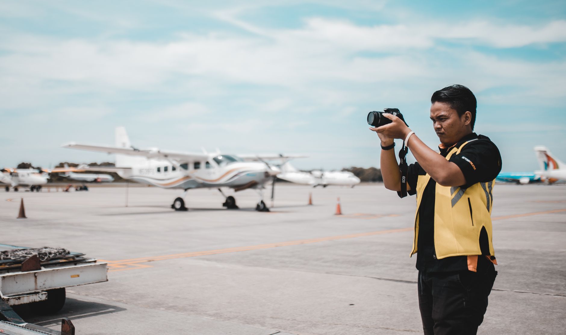 Asian man taking photos of planes on airport tarmac during the day.