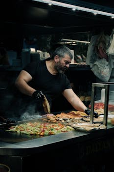 Man grilling vegetables in an outdoor market at night.