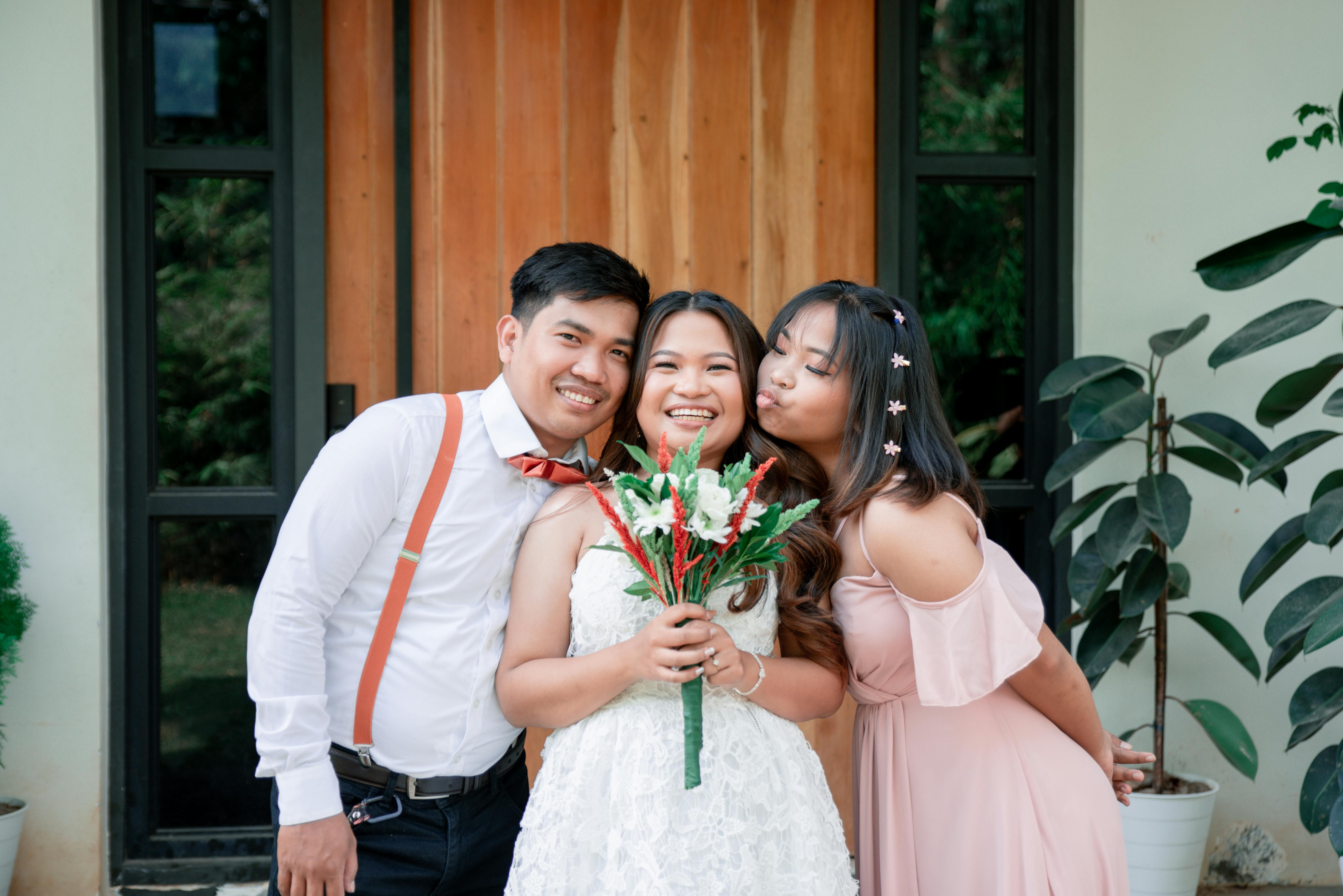 A bride, groom, and bridesmaid happily posing with a bouquet outdoors.