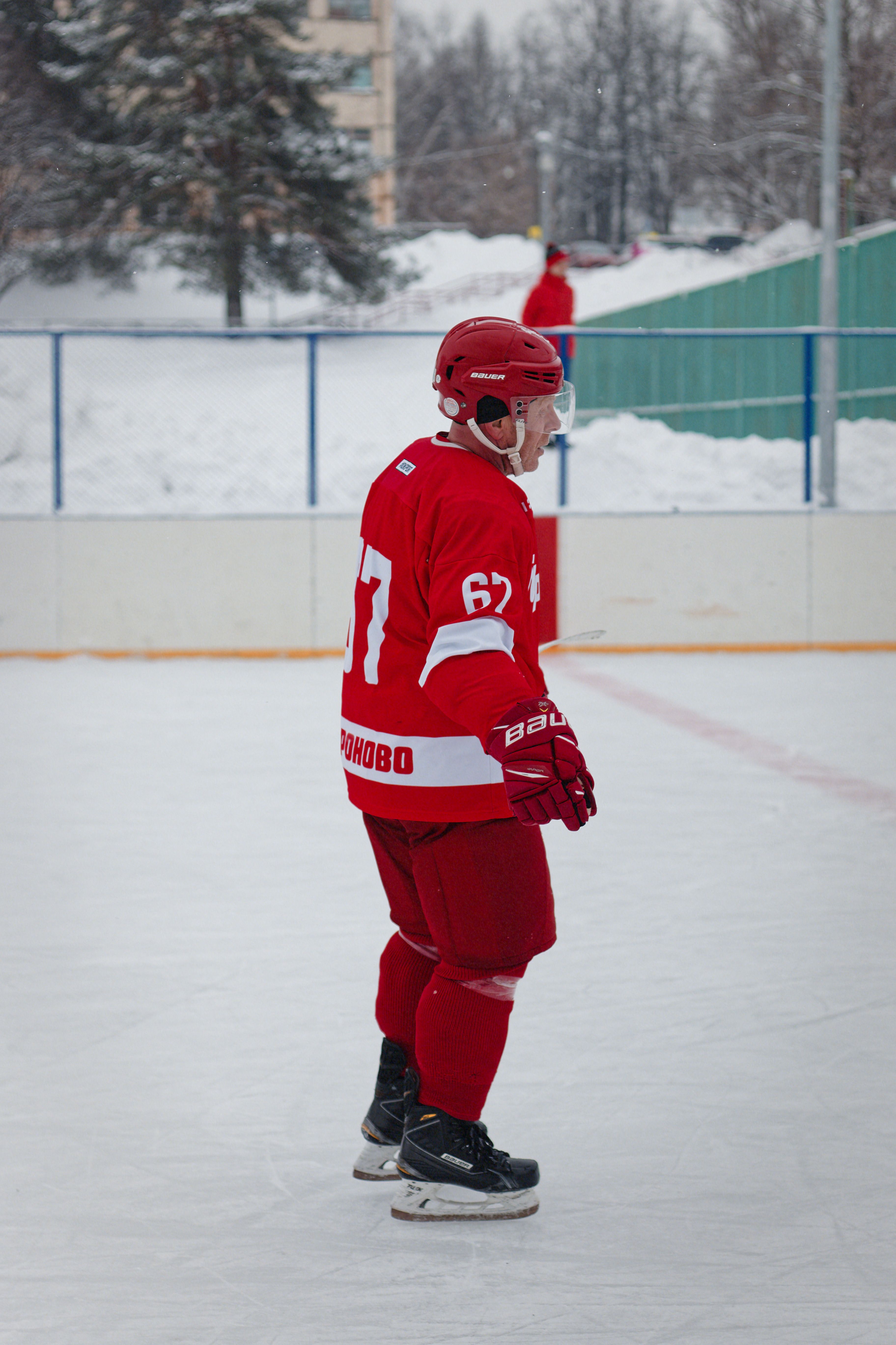 A hockey player in red gear stands on an outdoor ice rink during winter, ready for action.