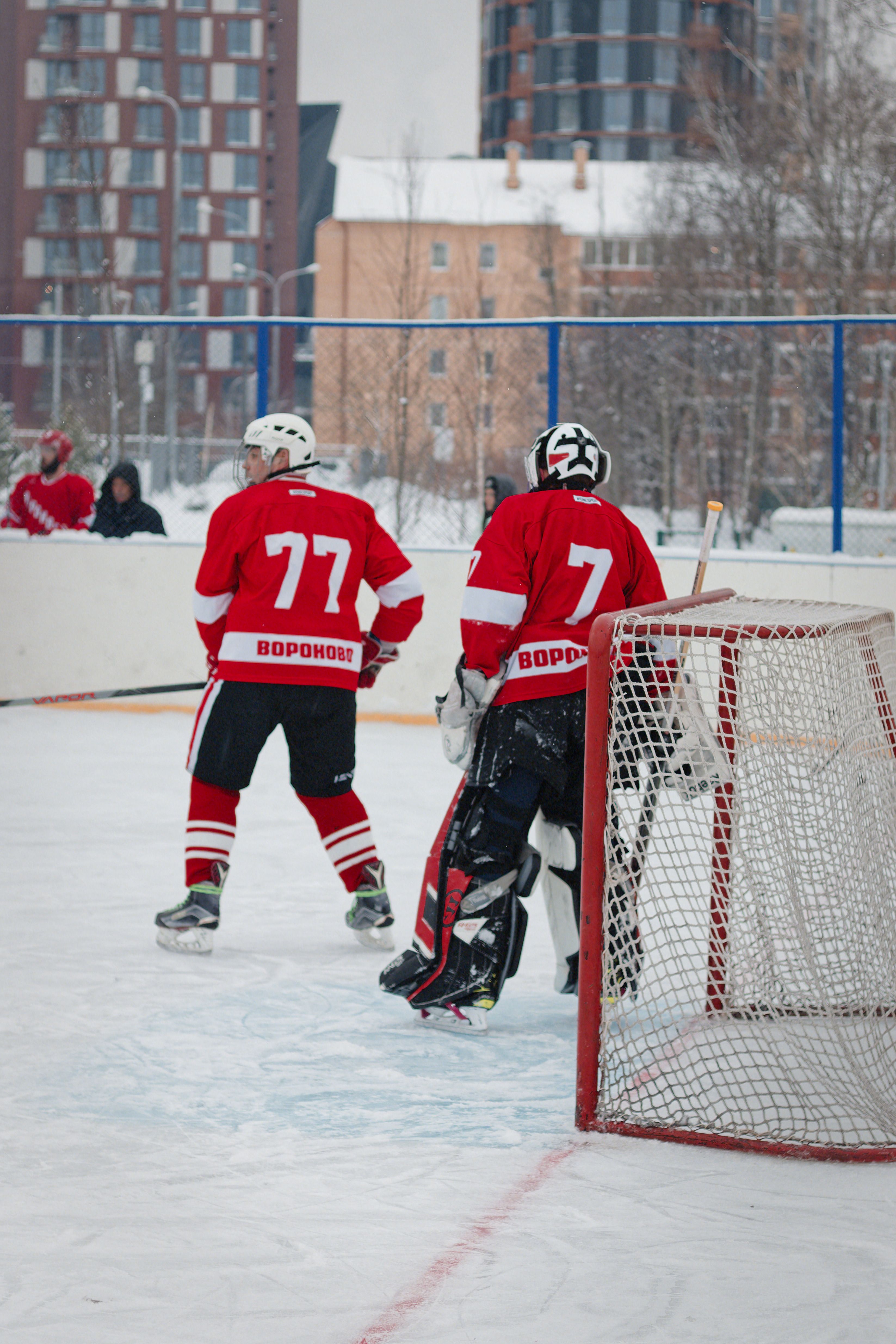 Two ice hockey players in red jerseys during a winter match outdoors.